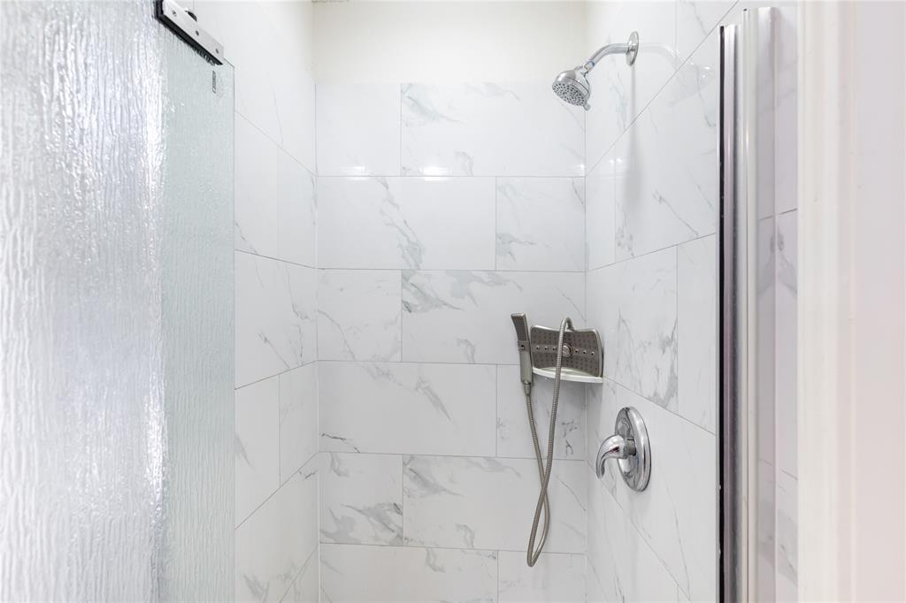 12680 Hillcrest Road, Unit 4101 Dallas, TX 75230 - Photo 22 of 37 Shower enclosure featuring large format white tiled walls with subtle gray veining, chrome fixtures, a handheld shower unit, and a textured glass shower door