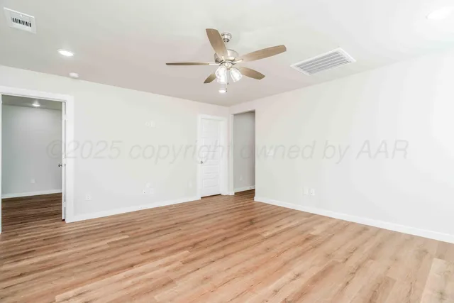 an empty room with wooden floor fan and windows