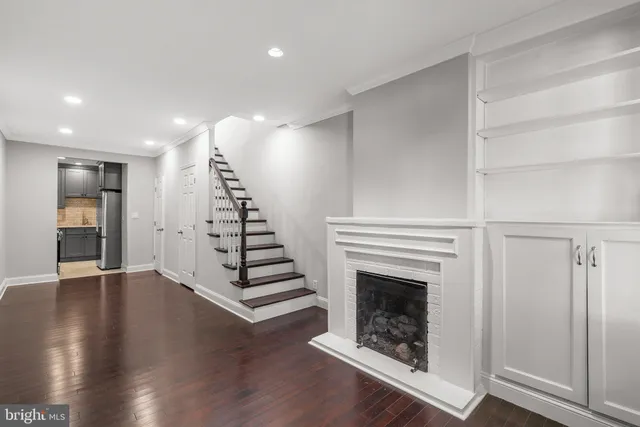 a view of an empty room with wooden floor staircase and a kitchen