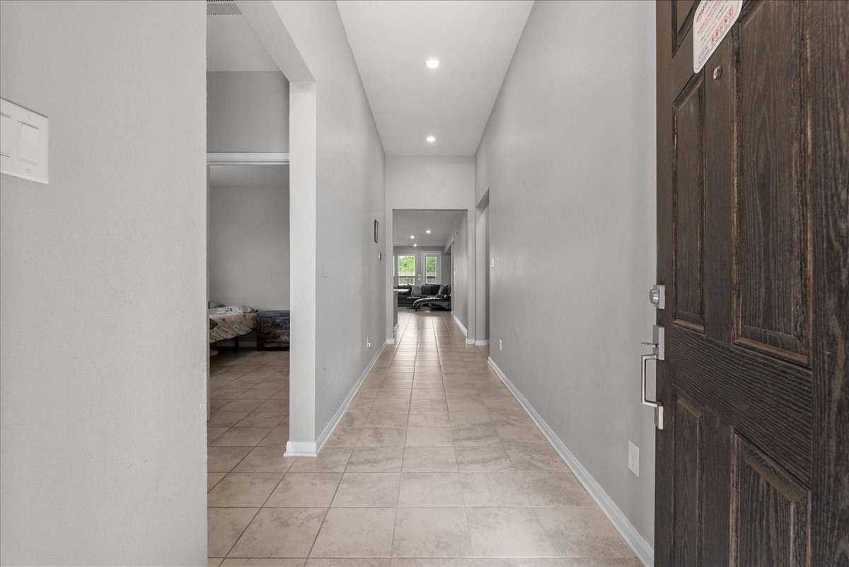 2320 Rosemary Street Rosenberg, TX 77469 - Photo 10 of 40 This photo shows a spacious, well-lit entry way, with tile flooring and neutral- painted walls. The hallway leads to an open concept living area with a glimpse of bedroom #1, and visible on the left, giving a welcoming and open feel.