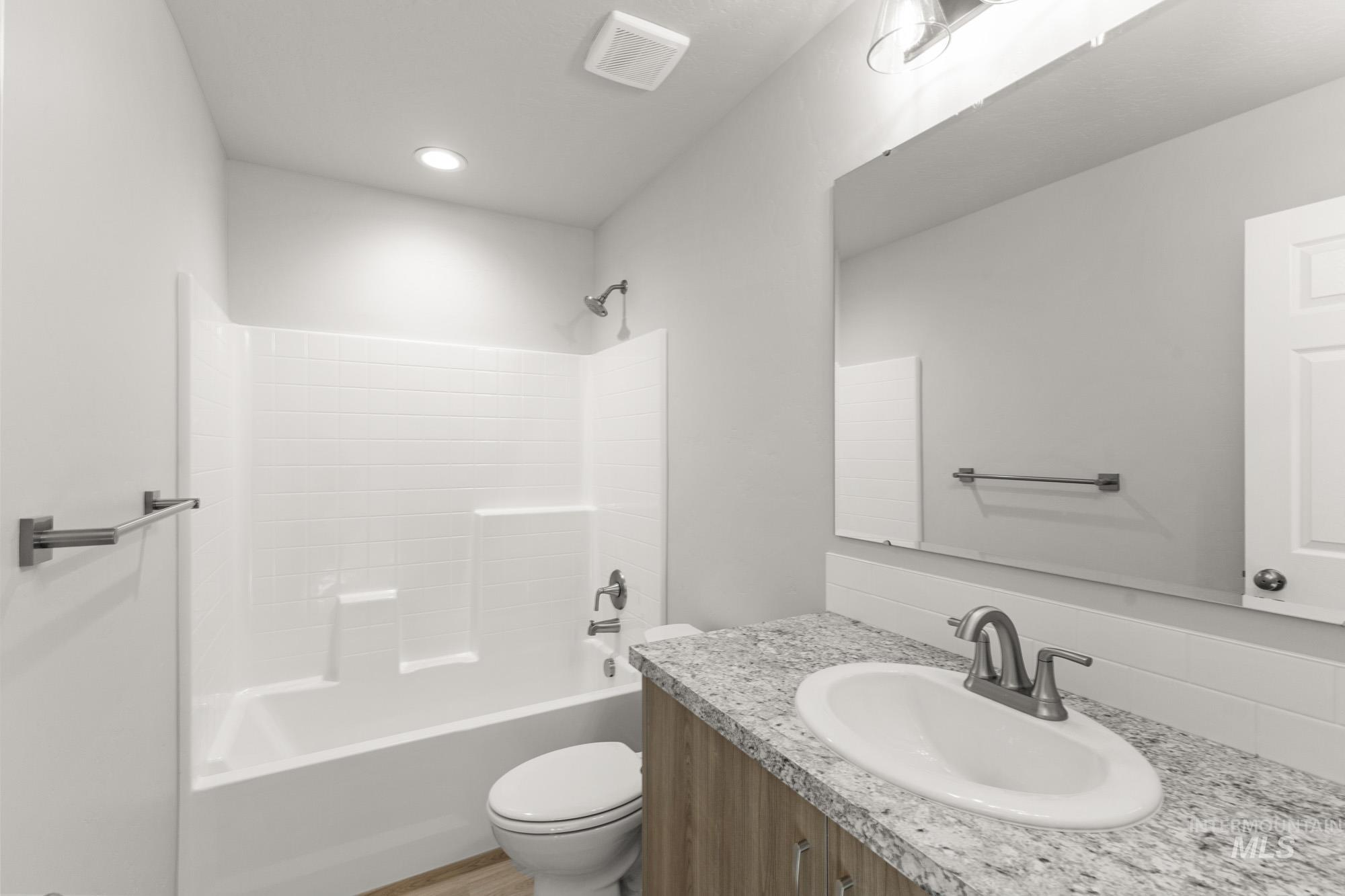 436 Merlin Court Middleton, ID 83644 - Photo 15 of 20 Bathroom featuring a white subway tile-patterned shower surround, a light wood-finish vanity with a speckled countertop, an undermount sink, and brushed nickel fixtures
