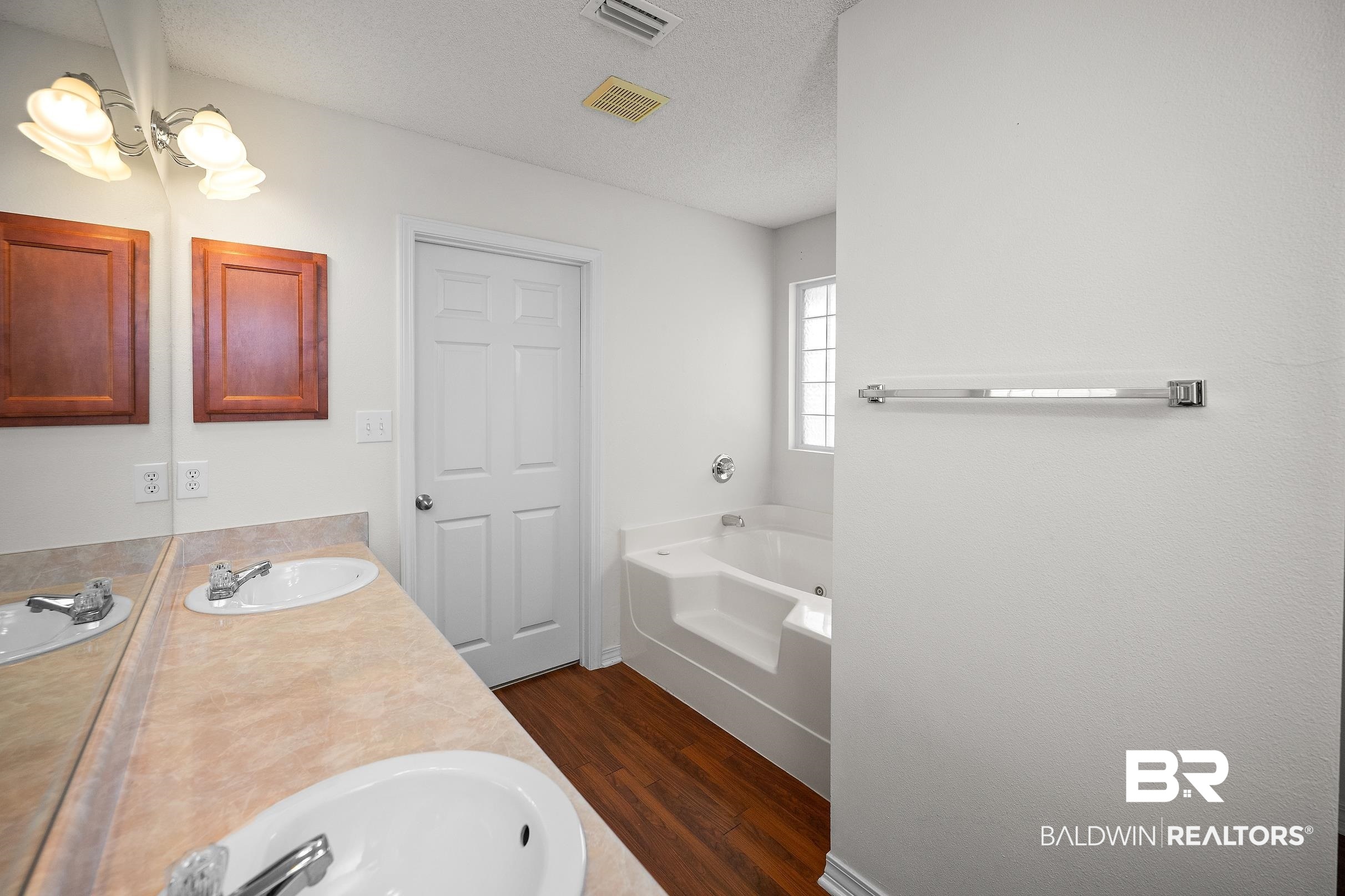 323 Manchester Lane Foley, AL 36535 - Photo 14 of 30 Bathroom featuring a dual-sink vanity with laminate countertop, wood-finish flooring, a built-in tub, and a privacy window