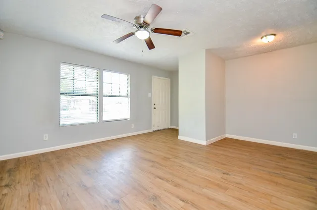 an empty room with wooden floor fan and windows