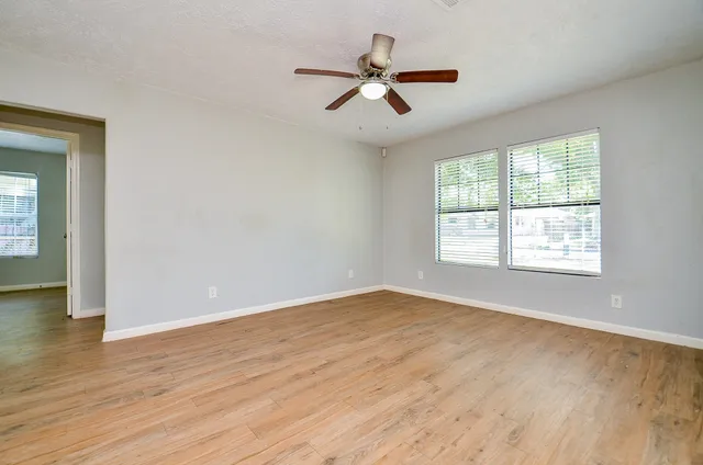 an empty room with wooden floor fan and windows