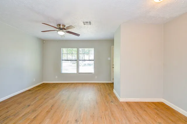 an empty room with wooden floor fan and windows