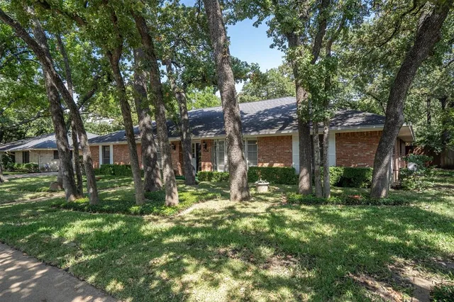 a view of house in front of a big yard with large trees and plants