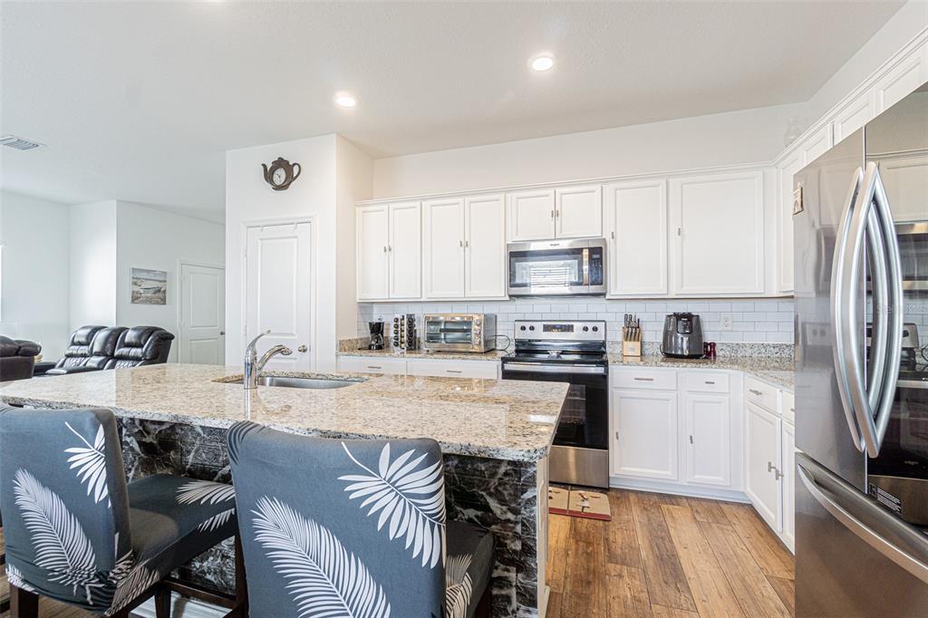 5265 Cricket Hill Road Brooksville, FL 34602 - Photo 15 of 30 a kitchen with stainless steel appliances granite countertop a stove top oven a sink dishwasher a dining table and chairs with wooden floor