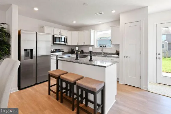 a kitchen with stainless steel appliances granite countertop a stove a sink a microwave a refrigerator white cabinets and wooden floor