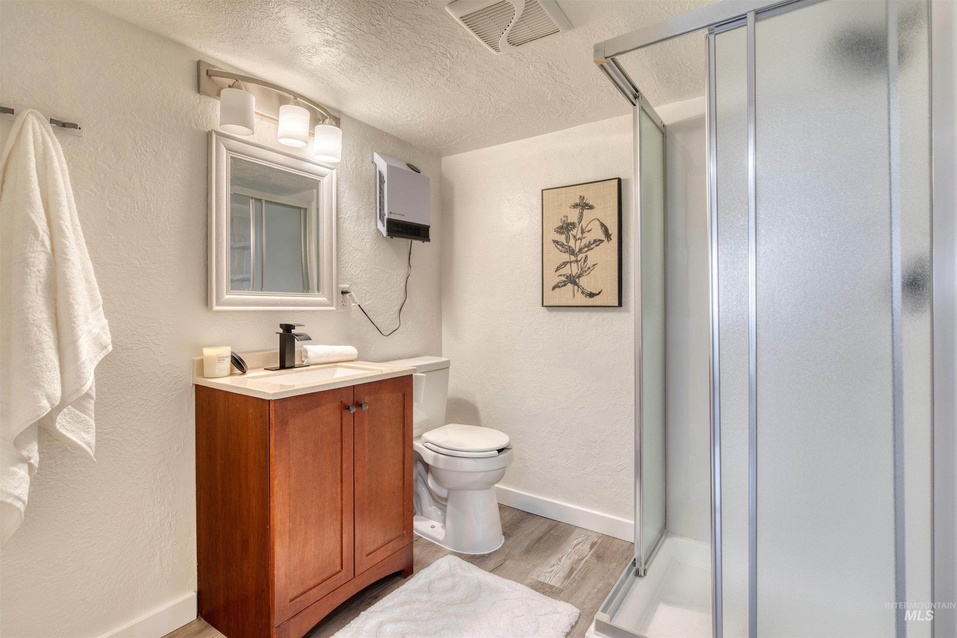 3311 West Hamilton Street Boise, ID 83705 - Photo 28 of 32 Bathroom with a textured wall, a textured ceiling, a shower stall, light wood-style floors, and vanity