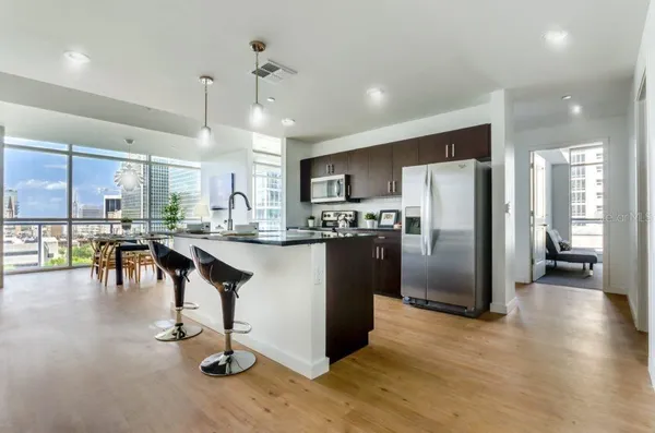 a kitchen with stainless steel appliances kitchen island granite countertop a refrigerator a stove a oven and a dining table with wooden floor