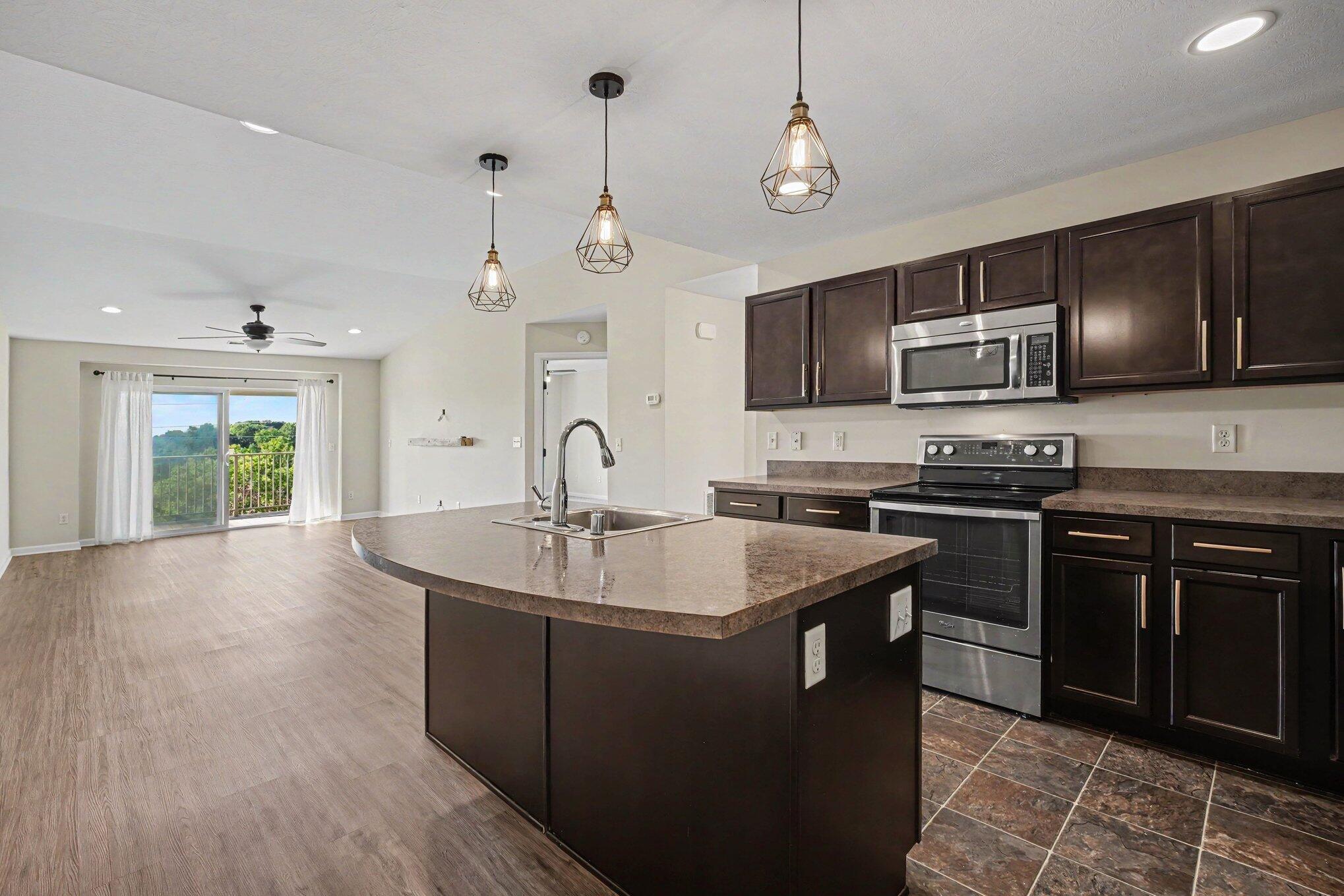 6069 Boulder View Cold Spring, KY 41076 - Photo 7 of 23 Open-concept kitchen and living area featuring a large center island with integrated sink, dark wood-finish cabinetry, stainless steel appliances, and pendant lighting