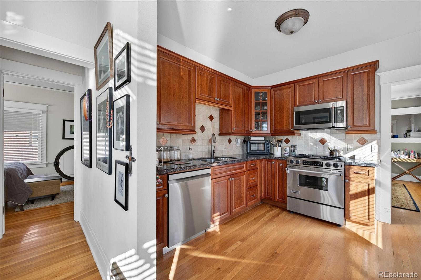 607 Madison Street Denver, CO 80206 - Photo 19 of 31 a kitchen with stainless steel appliances granite countertop a stove top oven a sink dishwasher a refrigerator and a dining table with wooden floor