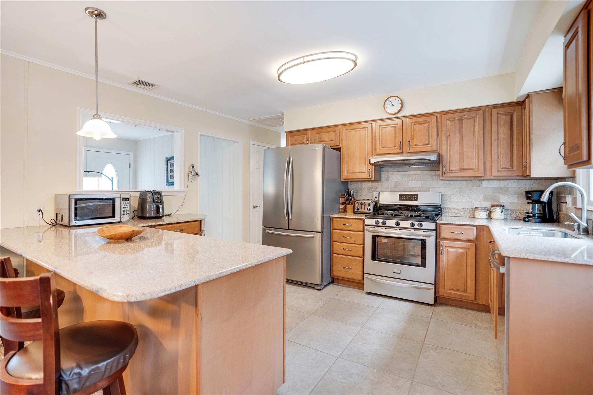 7 Russell Road Hampton Bays, NY 11946 - Photo 28 of 31 Kitchen featuring appliances with stainless steel finishes, light stone counters, a kitchen breakfast bar, a peninsula, and backsplash
