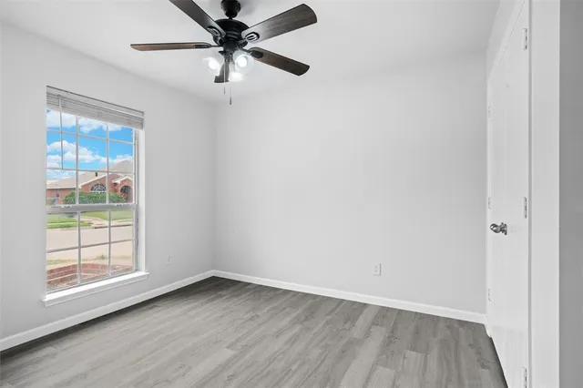 an empty room with wooden floor fan and windows
