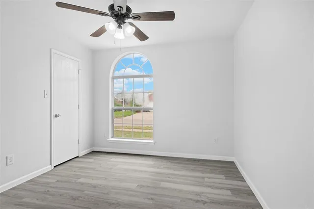 an empty room with wooden floor chandelier fan and windows