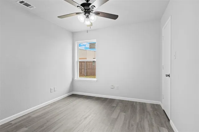 an empty room with wooden floor chandelier fan and windows