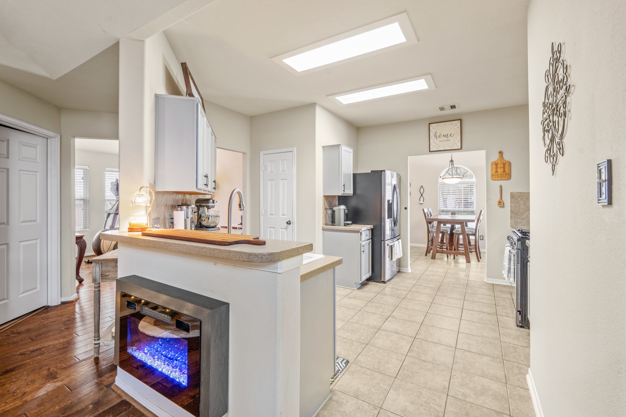 19646 Hardwood Ridge Trail Cypress, TX 77429 - Photo 7 of 22 At the center of the kitchen is a functional island with a breakfast bar, topped with light countertops and equipped with a modern sink and faucet. A built-in electric fireplace on the island adds a unique and cozy focal point, blending style with comfort.