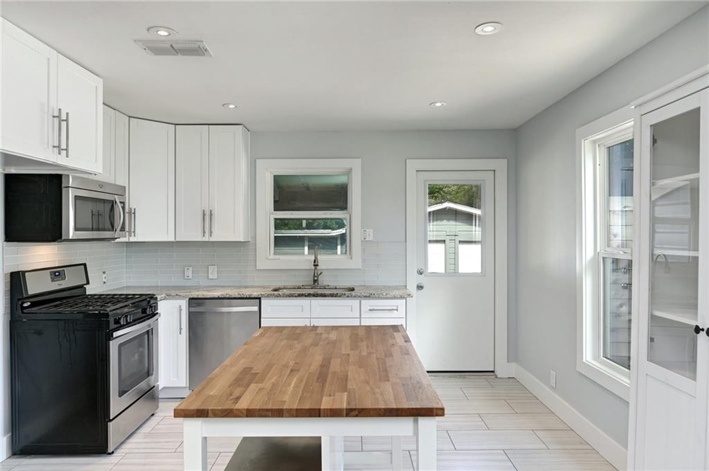 8318 Burrell Drive Austin, TX 78757 - Photo 7 of 27 Kitchen featuring appliances with stainless steel finishes, decorative backsplash, light stone counters, white cabinetry, and recessed lighting