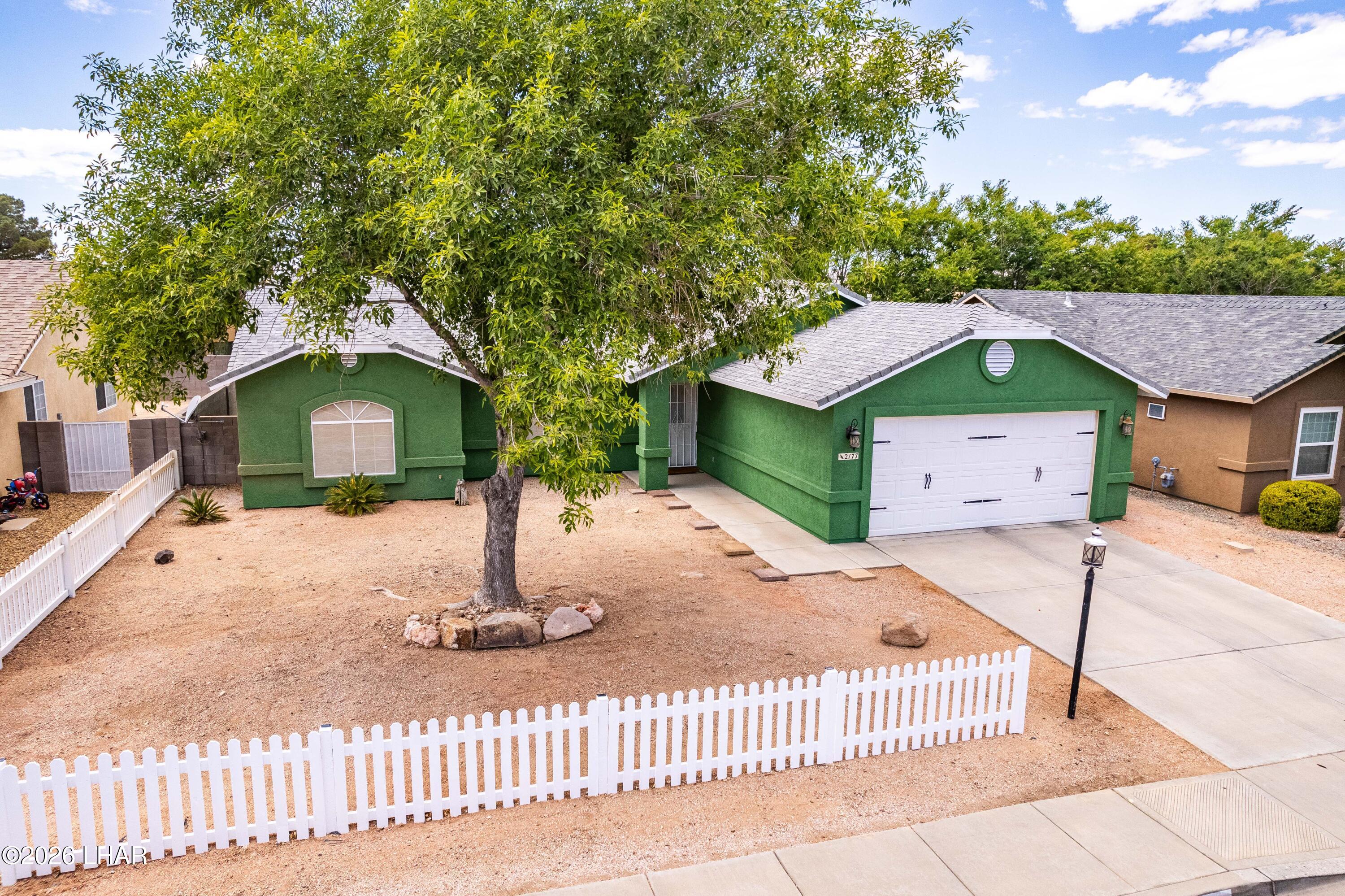 Single-story residential property featuring a green stucco exterior and a white picket fence