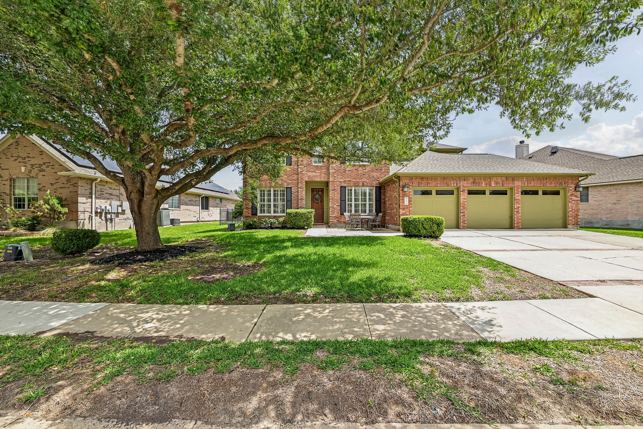 2408 Amen Corner Road Pflugerville, TX 78660 - Photo 3 of 40 Brick exterior residence featuring a three-car garage, mature front yard tree, and a concrete driveway