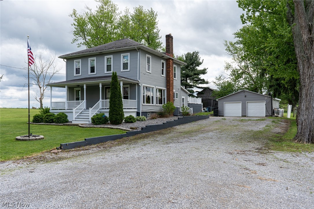 Gray-sided residence featuring a covered front porch with white railings, a prominent brick chimney, and a gravel driveway