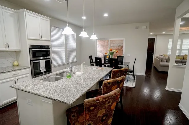 a kitchen with granite countertop a stove a sink a refrigerator and chairs