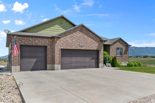 5702 950 North Ogden, UT 84404 - Photo 3 of 36 Brick facade residence featuring a two-car garage with panel doors, a concrete driveway, and a pitched roofline