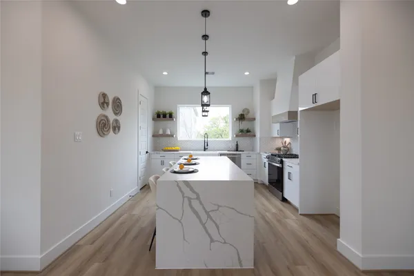 a large white kitchen with a refrigerator a stove a sink and a wooden floor