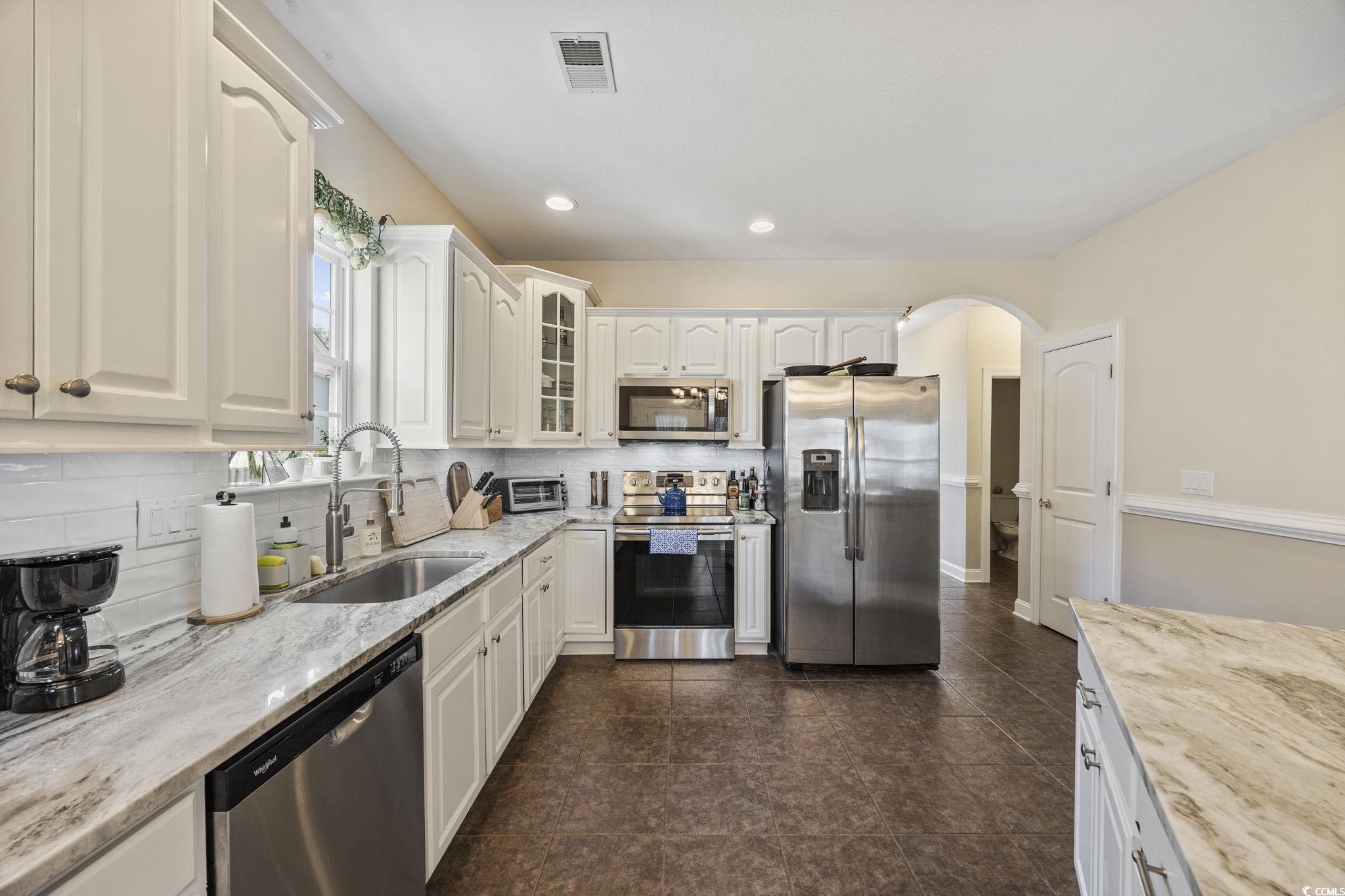 418 Cabo Loop Myrtle Beach, SC 29588 - Photo 9 of 40 Kitchen featuring light stone counters, appliances with stainless steel finishes, glass insert cabinets, backsplash, and white cabinets