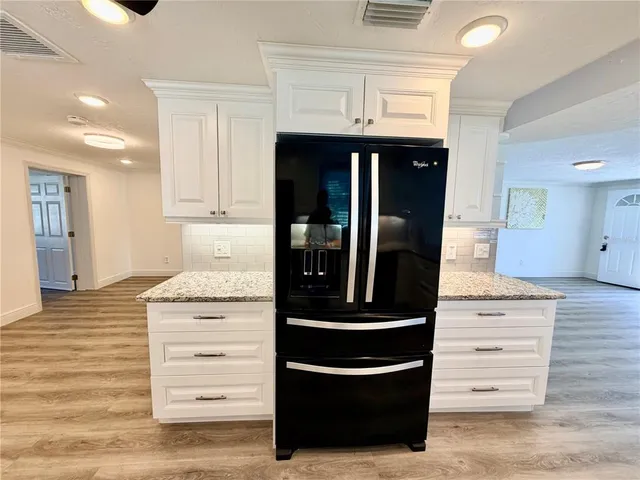 a large kitchen with stainless steel appliances kitchen island granite countertop a stove top oven a sink dishwasher and a refrigerator with wooden floor