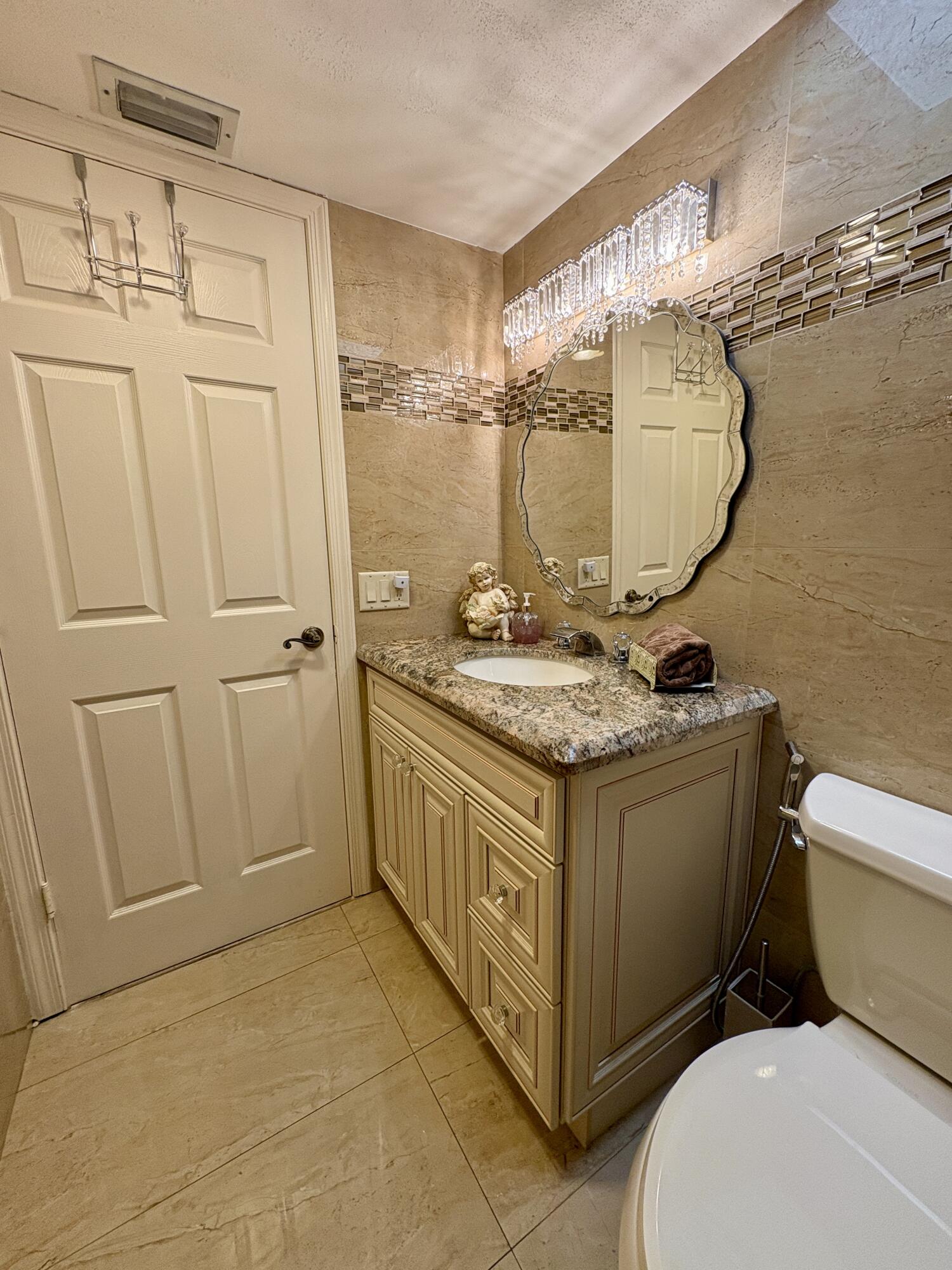 23249 Barwood Lane North, Unit 402 Boca Raton, FL 33428 - Photo 12 of 27 a bathroom with a granite countertop sink a toilet and a mirror
