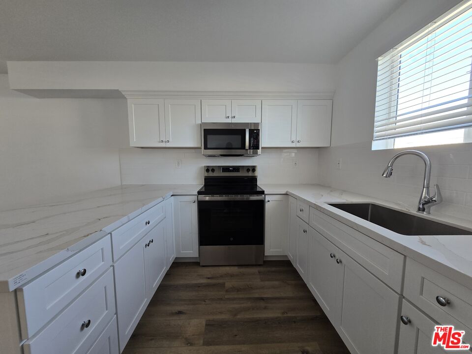 449 West 74th Street Los Angeles, CA 90003 - Photo 5 of 28 a kitchen with granite countertop white cabinets and black stainless steel appliances