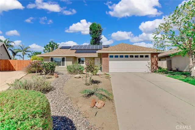 a view of a white house with a yard plants and large tree
