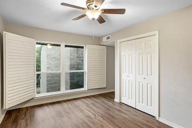 an empty room with wooden floor fan and windows