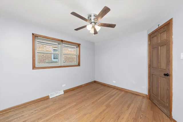 a view of an empty room with wooden floor and a ceiling fan