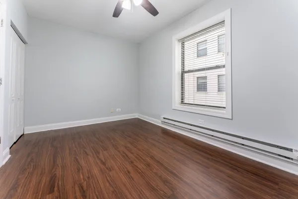 an empty room with wooden floor chandelier fan and windows