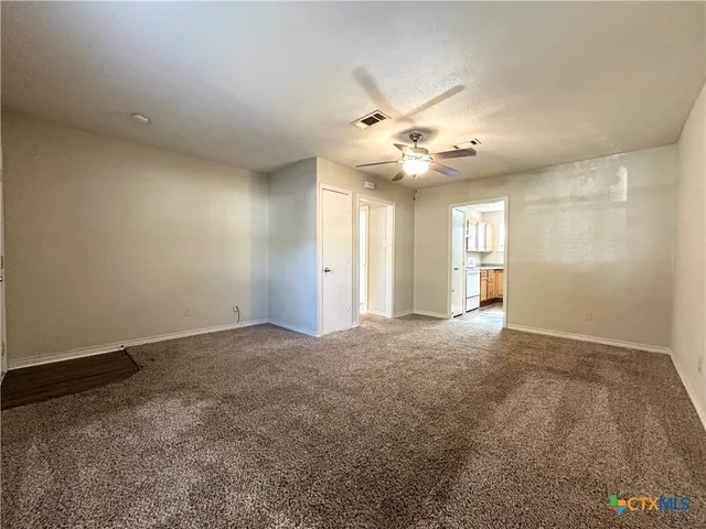 an empty room with chandelier fan and windows