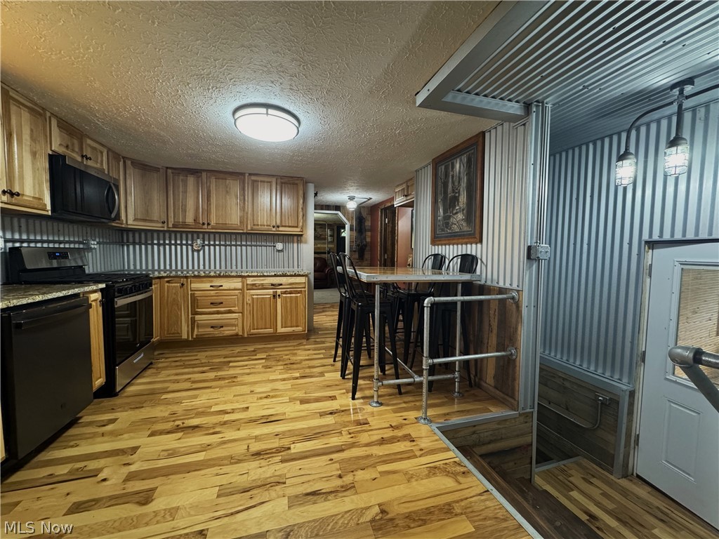 4421 State Road South Ashtabula, OH 44004 - Photo 9 of 18 Kitchen featuring light wood-finish cabinetry, black appliances, corrugated metal backsplash, granite-style countertops, and wood-finish flooring