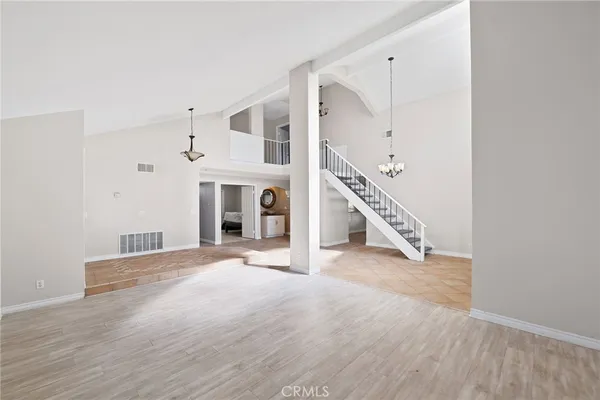 a view of an empty room with wooden floor stairs and a way to kitchen