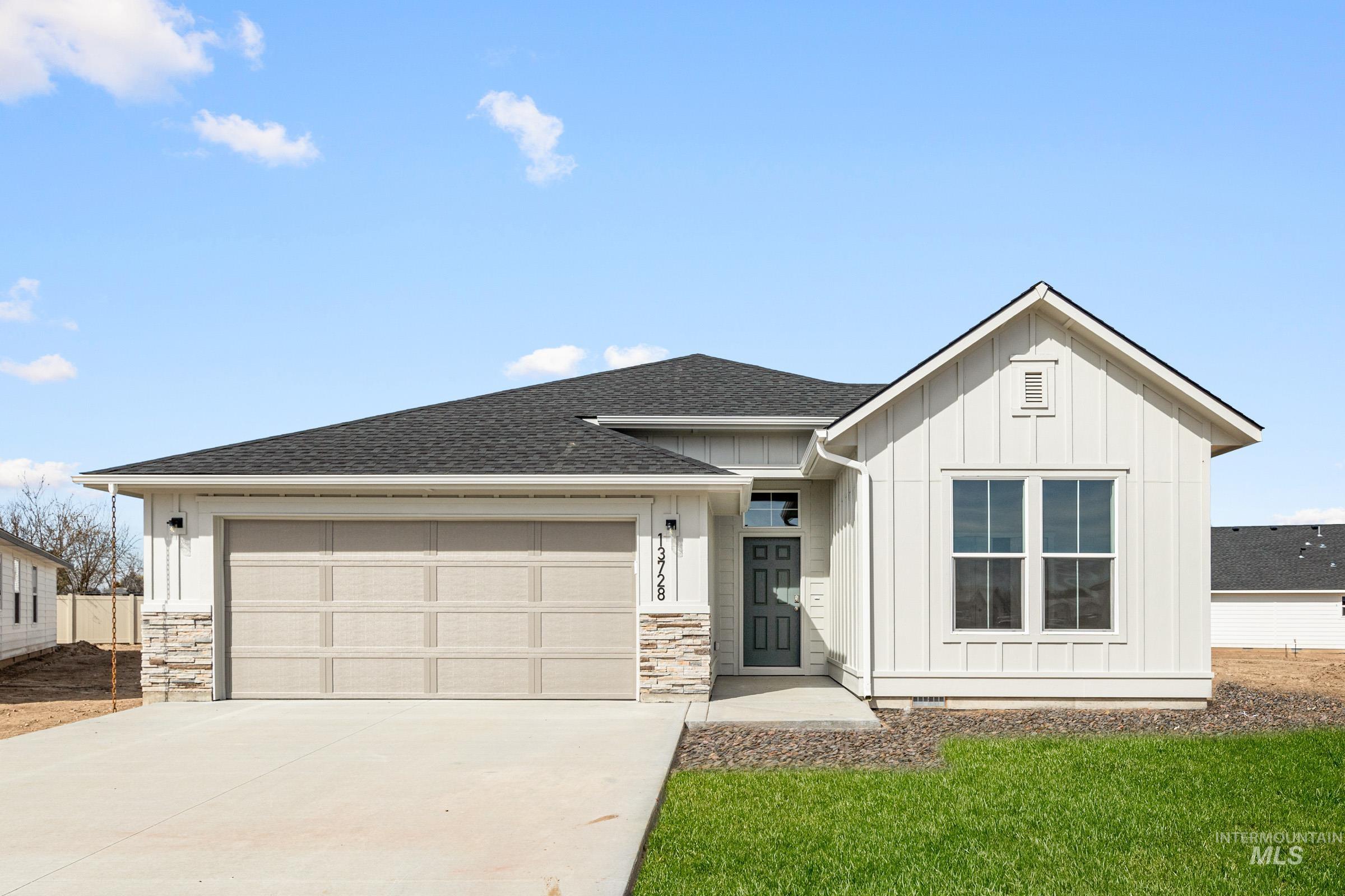 View of front facade with board and batten siding, roof with shingles, a garage, concrete driveway, and a front lawn