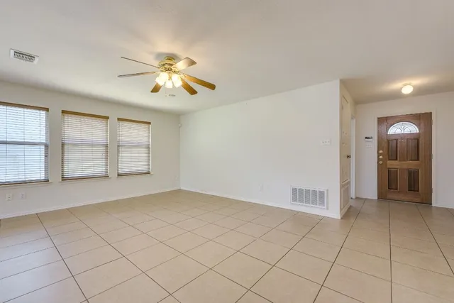 an empty room with chandelier fan and kitchen view