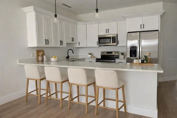 a kitchen with stainless steel appliances granite countertop a sink a stove a refrigerator with white cabinets and wooden floor