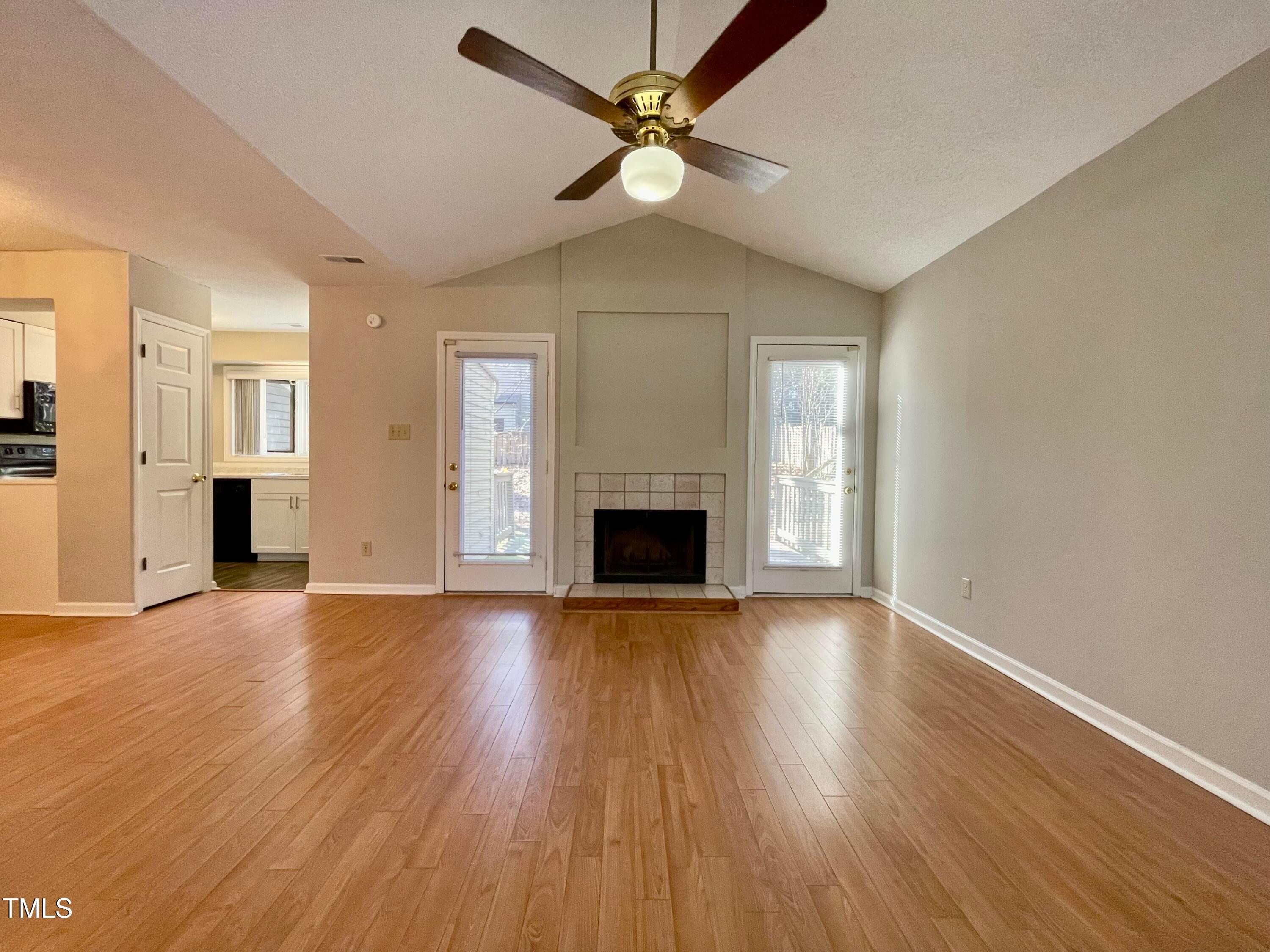 4114 Beechnut Lane Durham, NC 27707 - Photo 3 of 25 an empty room with wooden floor a ceiling fan a fireplace and windows