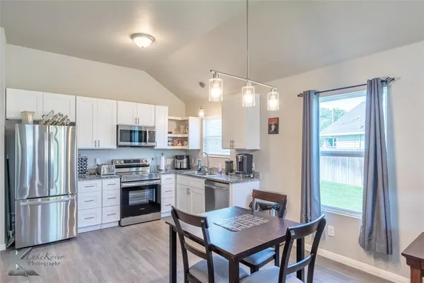 a kitchen with stainless steel appliances a dining table chairs stove refrigerator and cabinets