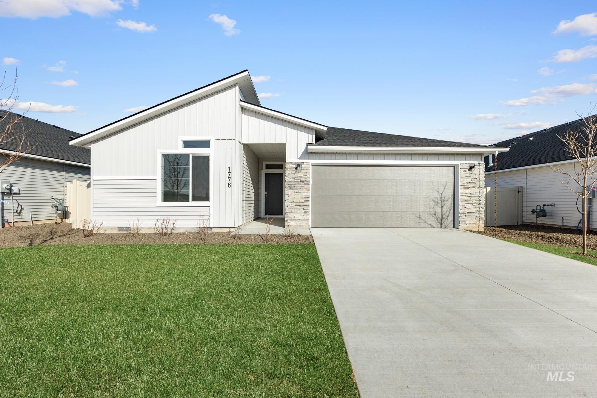 View of front of house featuring board and batten siding, an attached garage, a front yard, driveway, and stone siding