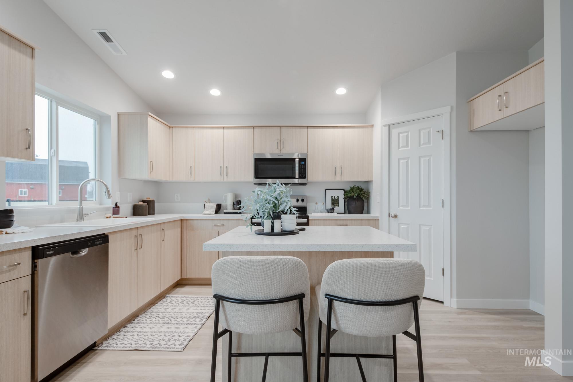 1776 West Unforgettable Street Meridian, ID 83642 - Photo 6 of 28 Kitchen featuring light brown cabinetry, a breakfast bar area, appliances with stainless steel finishes, a center island, and light wood finished floors