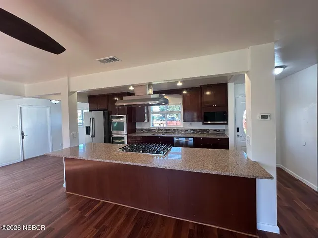 a view of a room with kitchen island stainless steel appliances wooden floor and living room view