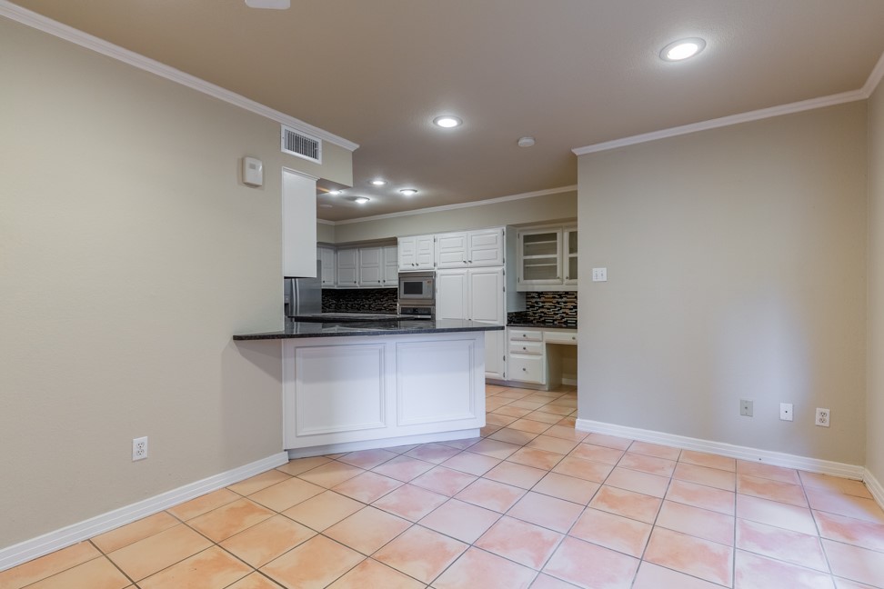 10907 Legends Lane Austin, TX 78747 - Photo 14 of 35 Kitchen featuring light tile patterned floors, a peninsula, dark countertops, decorative backsplash, and white cabinetry