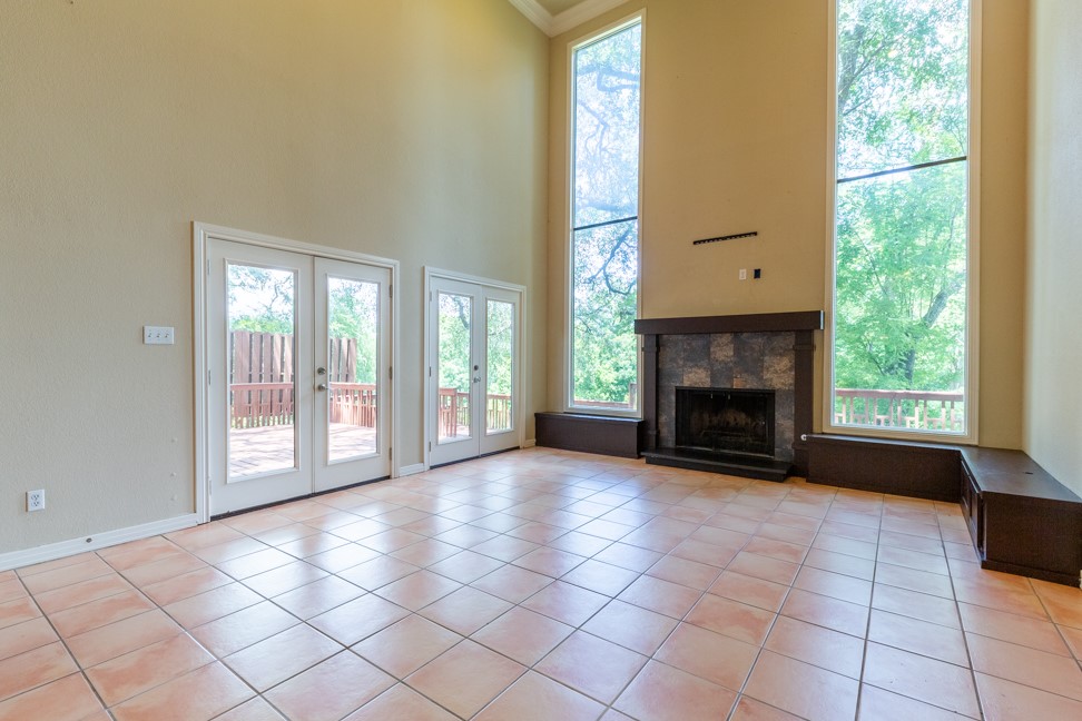 10907 Legends Lane Austin, TX 78747 - Photo 5 of 35 Unfurnished living room featuring french doors, light tile patterned flooring, a towering ceiling, a fireplace, and crown molding