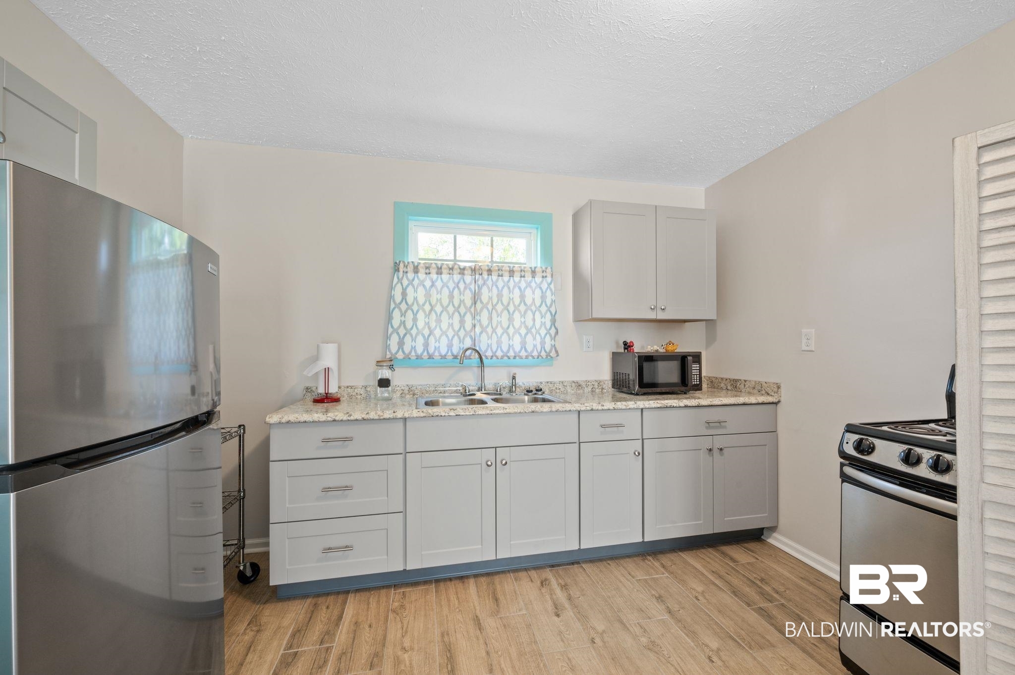 48513 Phillipsville Road Bay Minette, AL 36507 - Photo 39 of 50 Kitchen with stainless steel appliances, light wood finished floors, gray cabinetry, a textured ceiling, and light stone counters